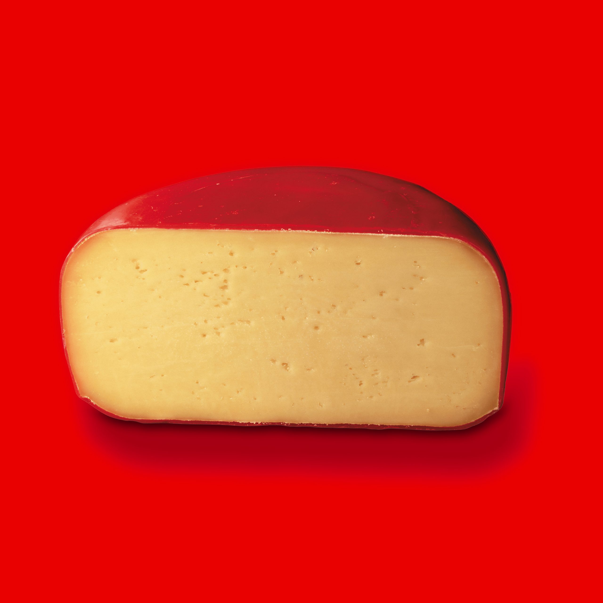 Half a wedge of cheese with red wax over red background
