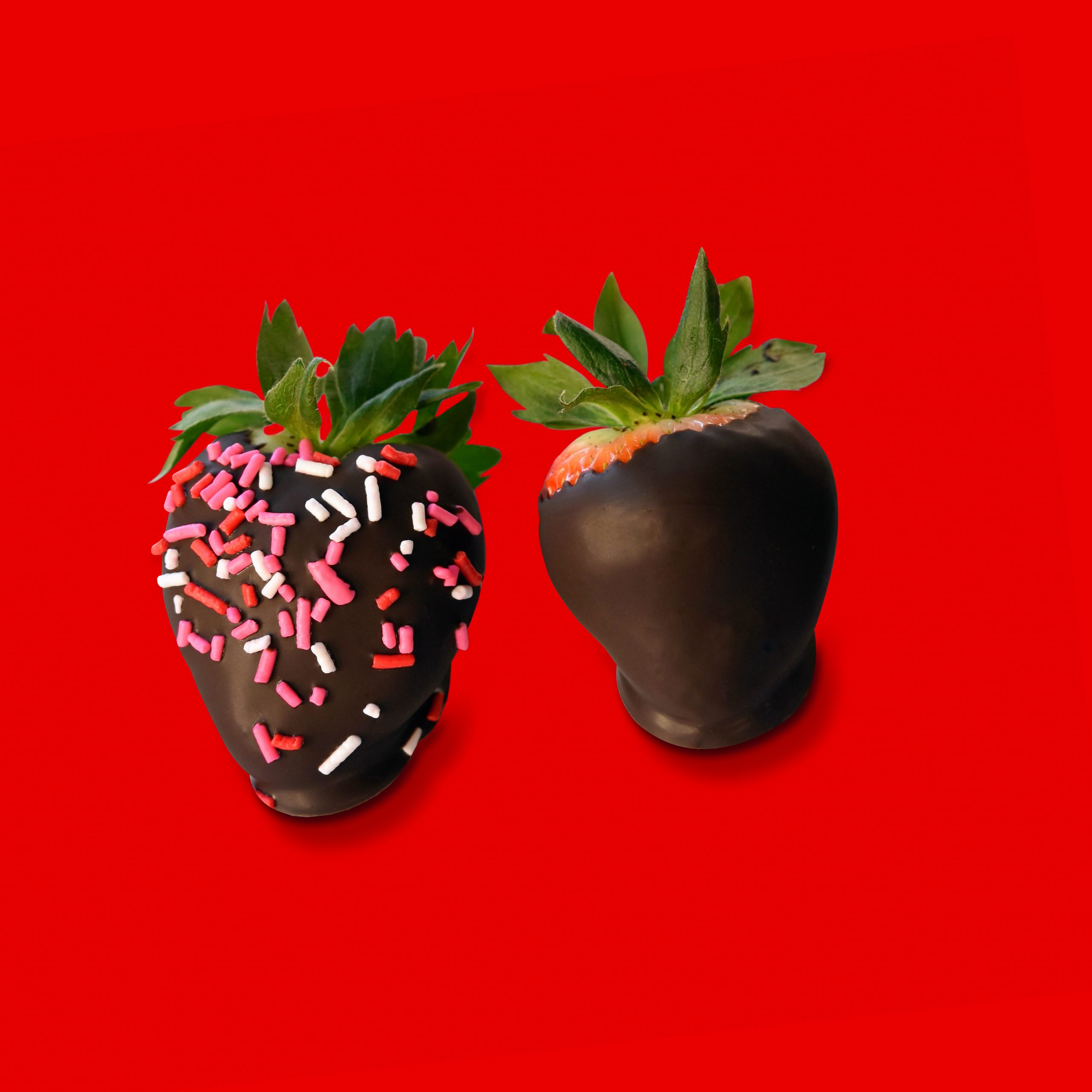 Two chocolate covered strawberries with sprinkles over read background